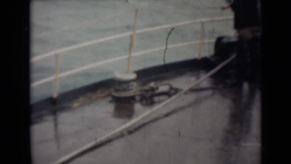 1946 India 8mm frame with a blurred figure at the edge of a rain-slick deck beside railings, a bollard, and coiled line.