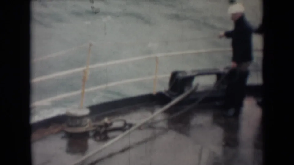 1946 8mm shipboard footage near India per metadata, showing coated men on a wet deck with railings, rope, and rough sea behind them.