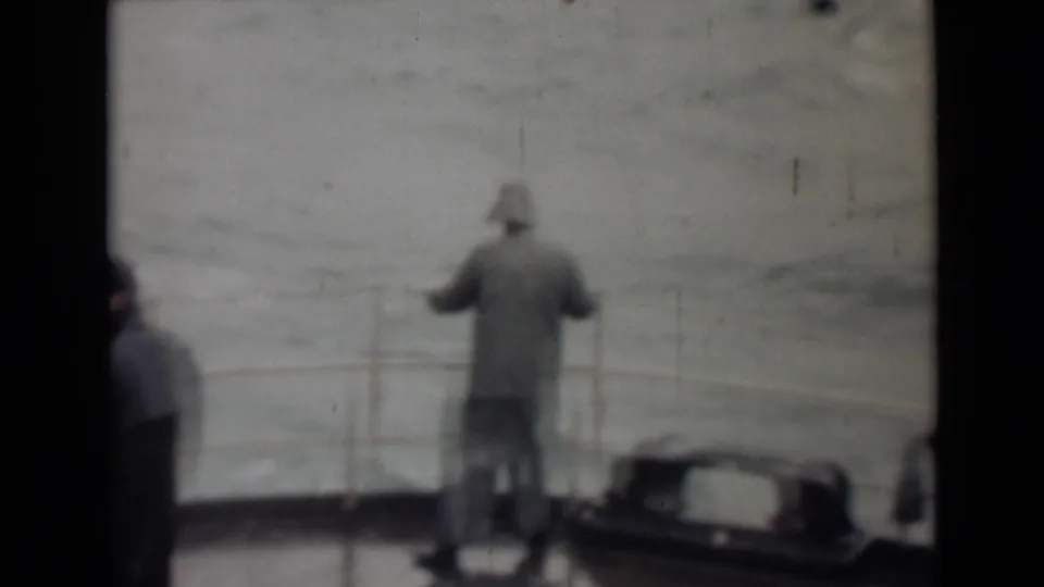 1946 8mm maritime footage near India per metadata, with a lone coated figure facing the sea from a wet deck railing.