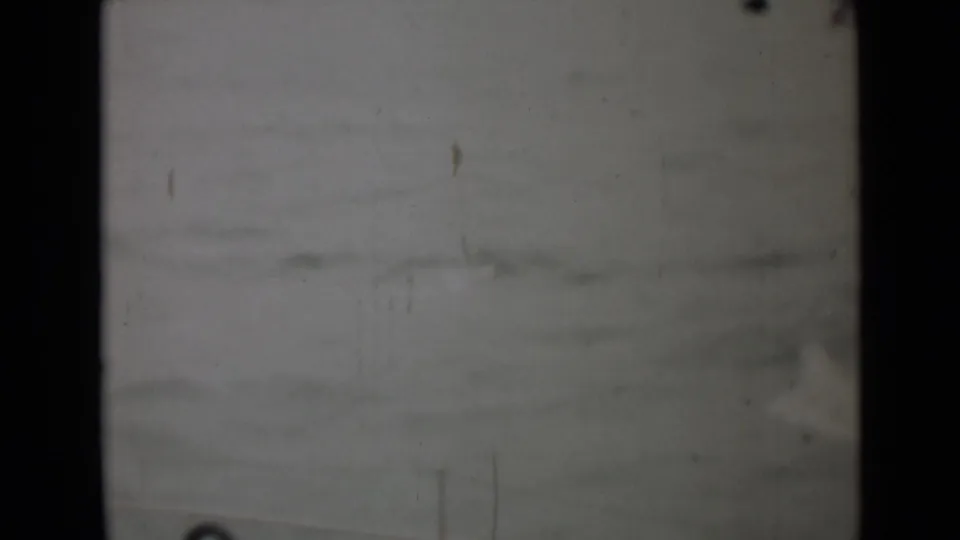 A soft, worn 8mm view of choppy water, with a faint human figure or deck edge near the right side.