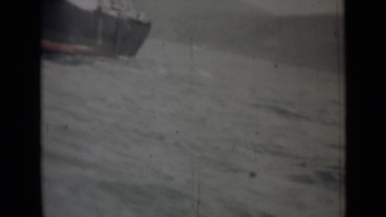 1946 India 8mm frame with the bow of a dark vessel entering the shot over choppy gray water.