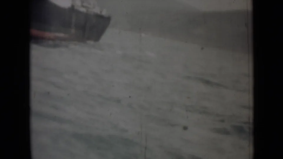 1946 India 8mm frame with the bow of a dark vessel entering the shot over choppy gray water.