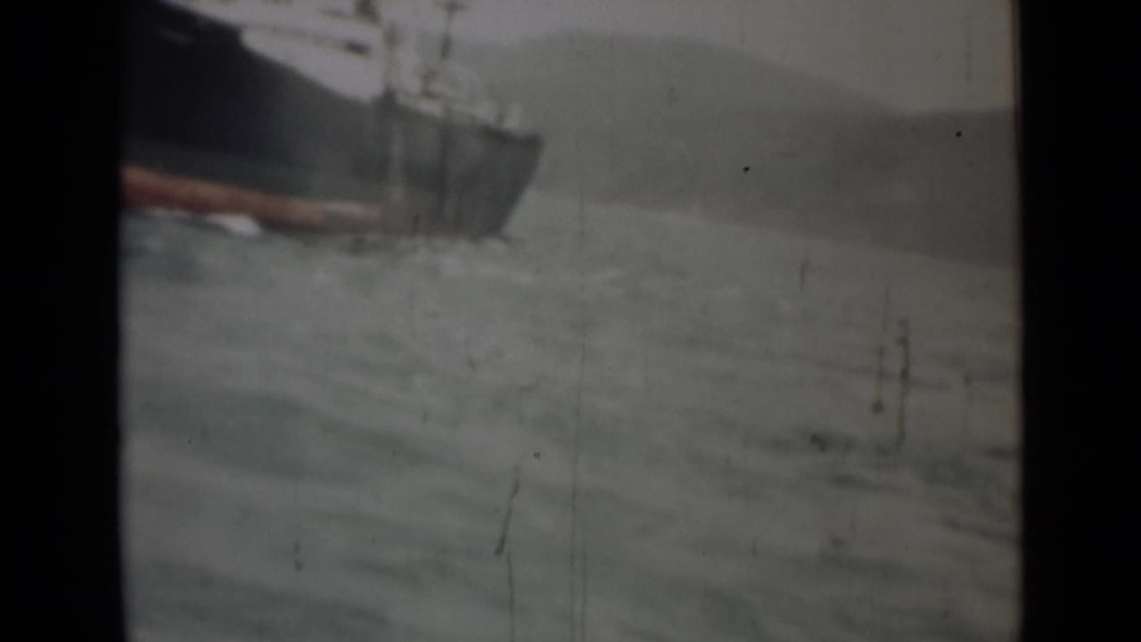 Cargo ship partly cropped at left moving through choppy water under a hazy sky.