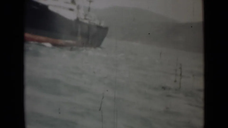 1946 India 8mm frame showing a dark cargo ship partially cropped beside rough water and a faint shoreline.