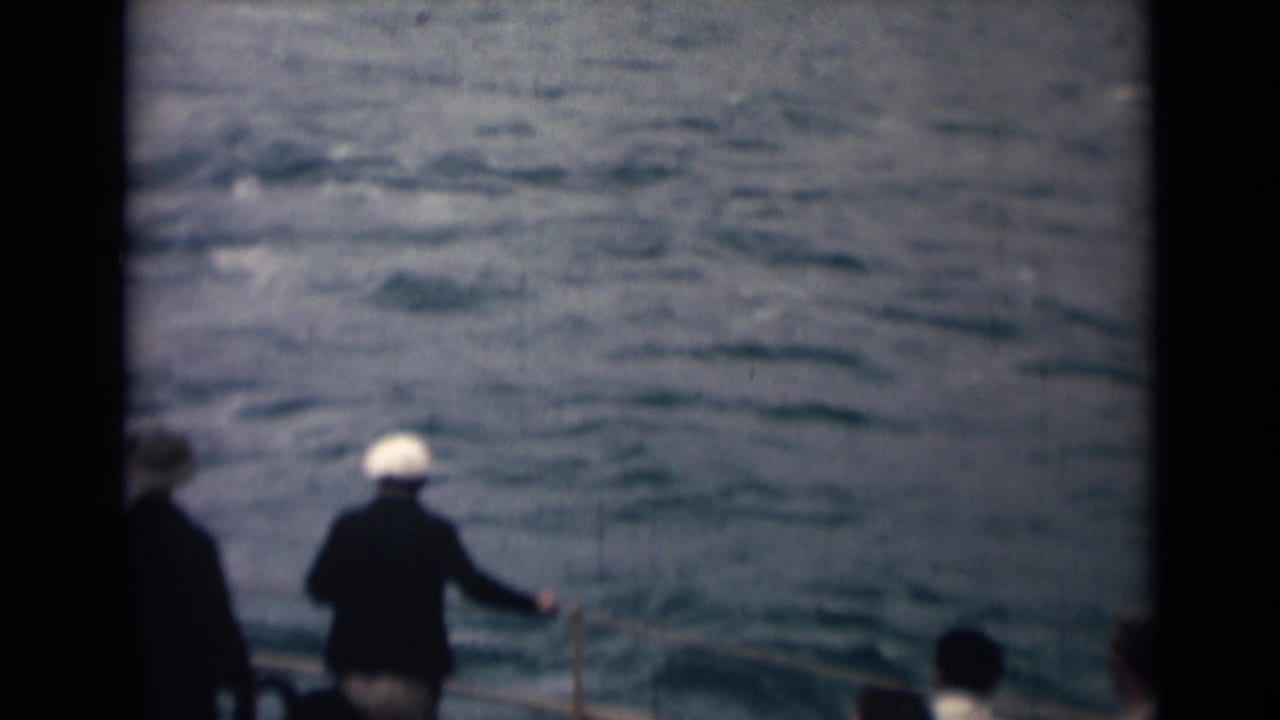 1946 India 8mm frame of sailors on deck, including a white-capped figure at the rail looking out over choppy water.