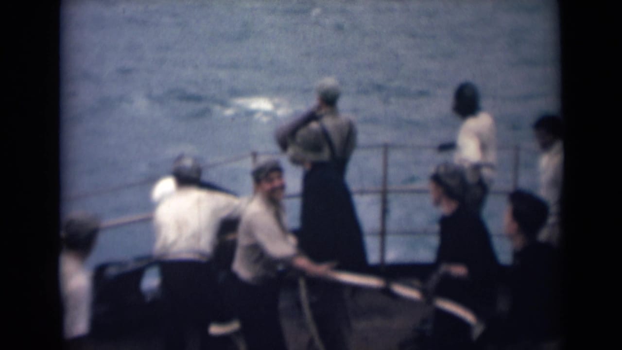 1946 India 8mm frame showing men in light shirts and caps pulling or handling a line on a boat deck beside choppy water.