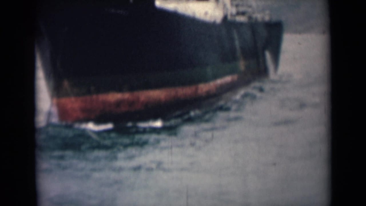 1946 India 8mm frame showing the side of a dark boat hull, red lower paint, water below and partially visible people above.