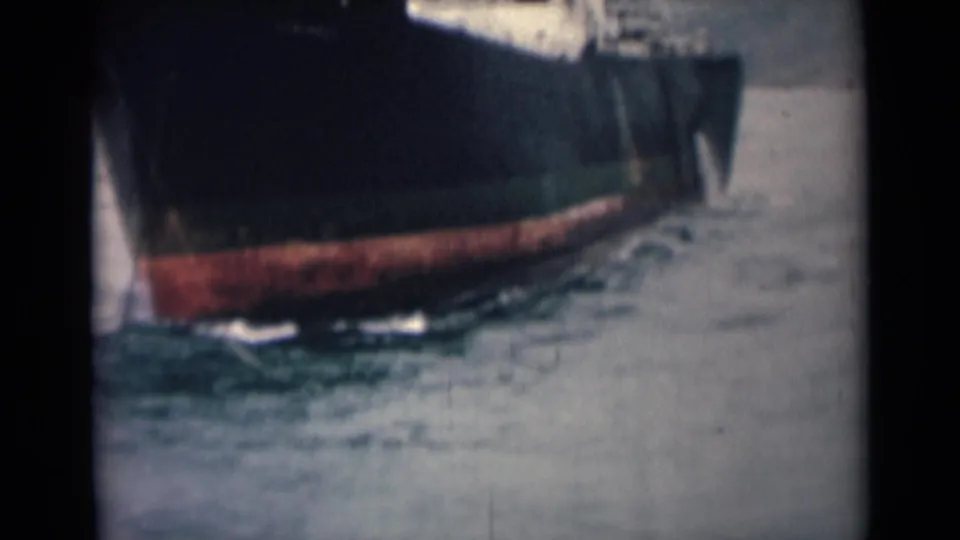 1946 India 8mm frame showing the side of a dark boat hull, red lower paint, water below and partially visible people above.