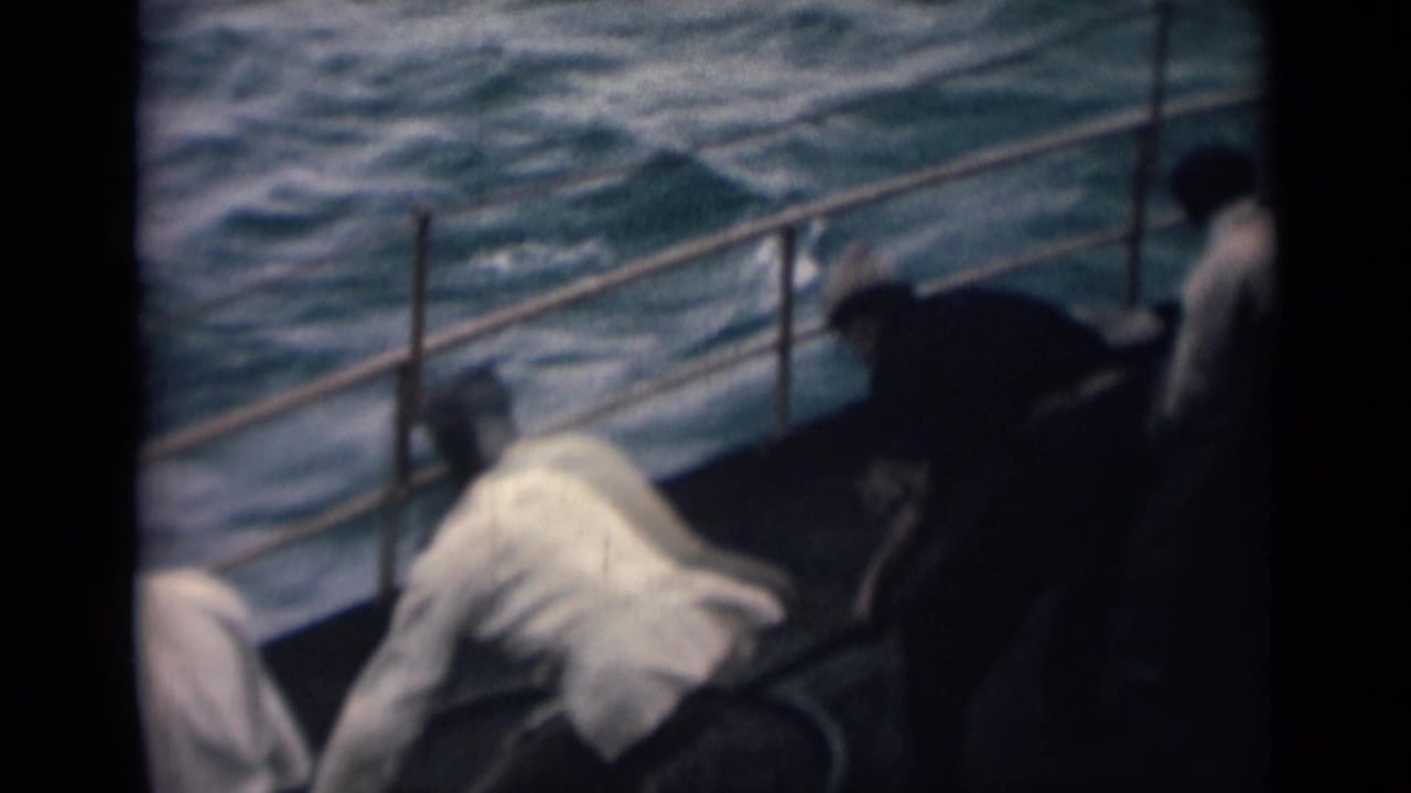 Men lean over a boat deck near railings while rough sea water moves beside the hull.