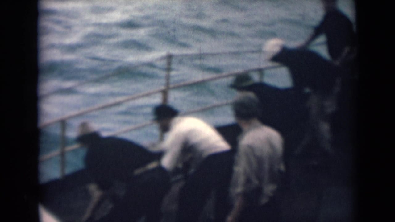 Several men gather at the side of a boat, bending toward a rope or deck fitting near the water.