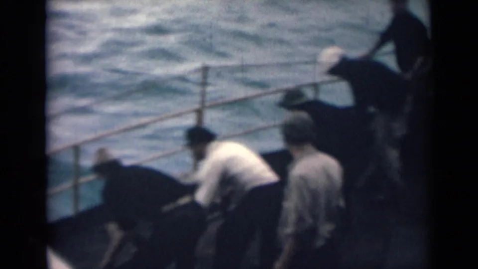 India 1946 8mm frame with men in light shirts and caps clustered on a boat deck beside choppy sea water.