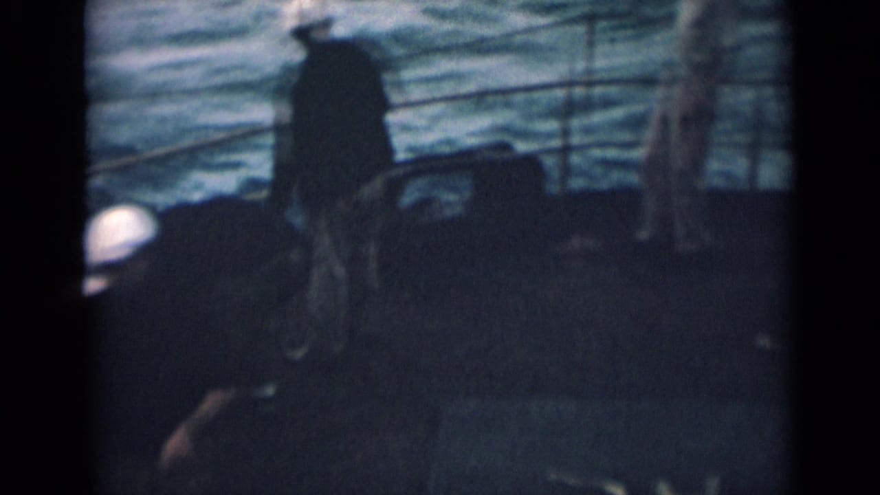 Dark ship deck with a sailor in a white cap and open water beyond the railings.