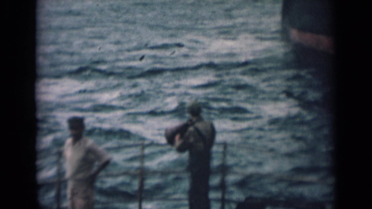 1946 India home-movie frame with sailors standing and moving on a ship deck beside railings and open water.