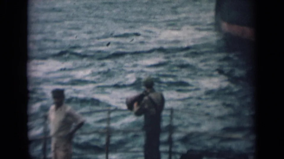 1946 India home-movie frame with sailors standing and moving on a ship deck beside railings and open water.