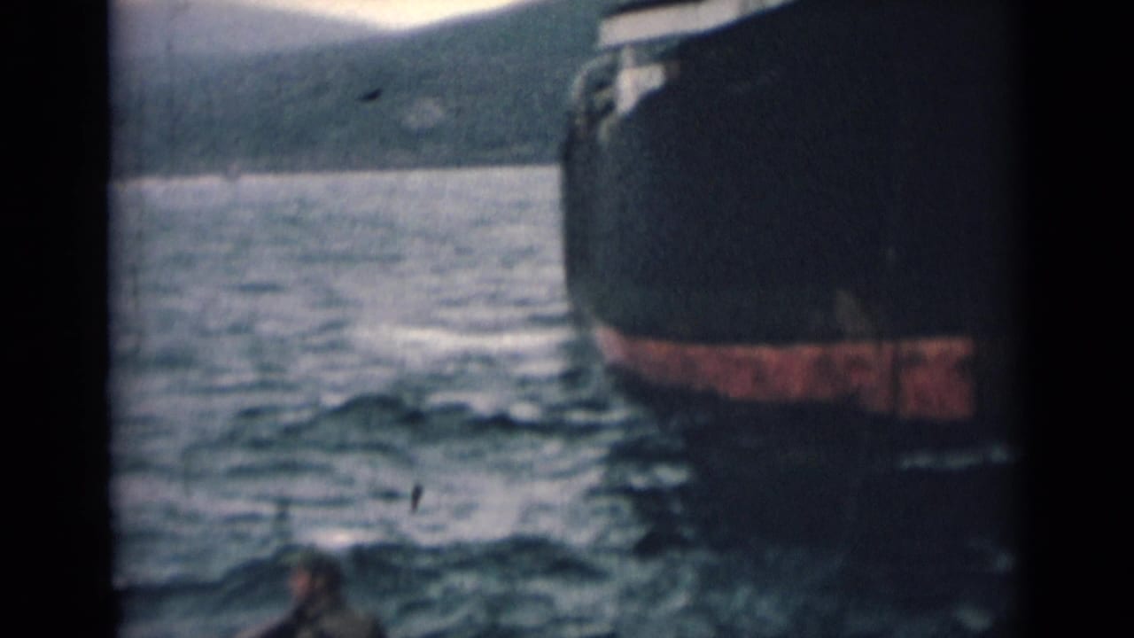 1946 India maritime frame showing a ship hull beside open water, with hazy landforms visible in the distance.
