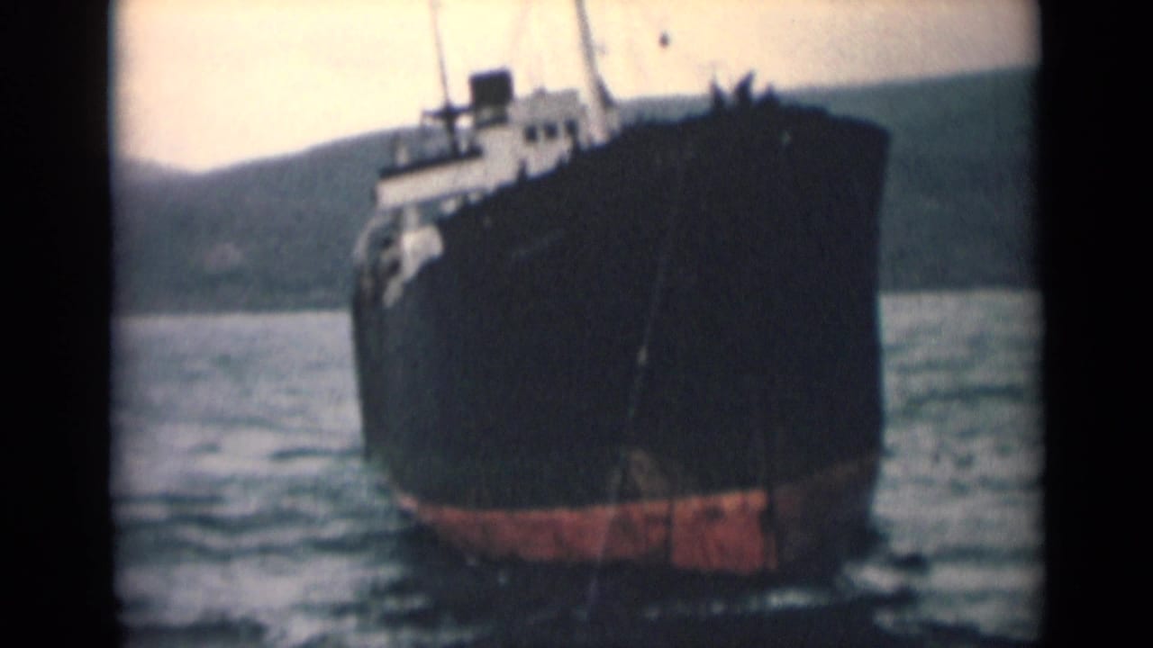 Dark ship bow and red lower hull visible on calm water near low hills.
