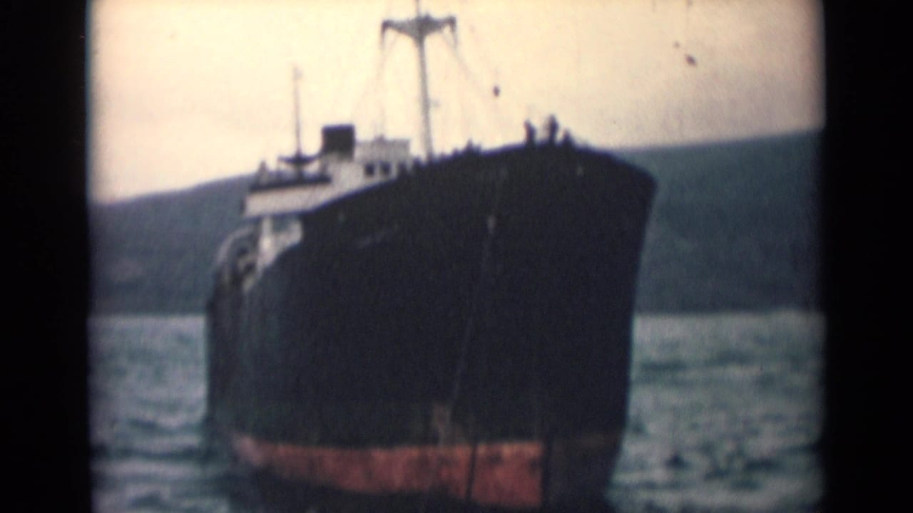 1946 India 8mm frame showing the vessel close to camera, with a dark hull, red lower band, and coastal background.