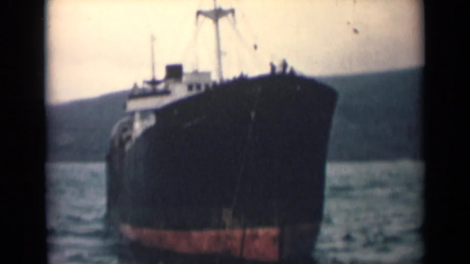 1946 India 8mm frame showing the vessel close to camera, with a dark hull, red lower band, and coastal background.