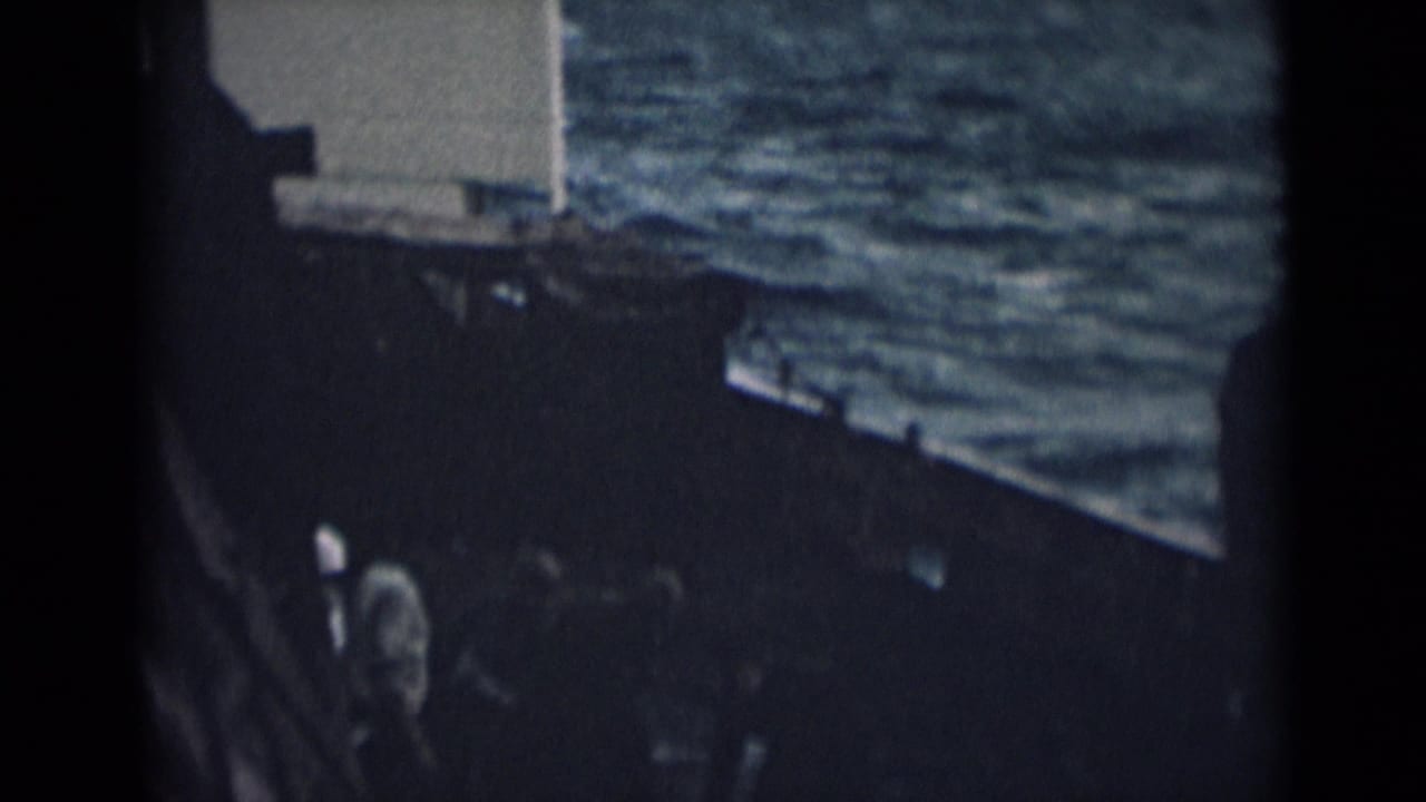 Dark ship deck beside choppy water with railings and partial ship structure.