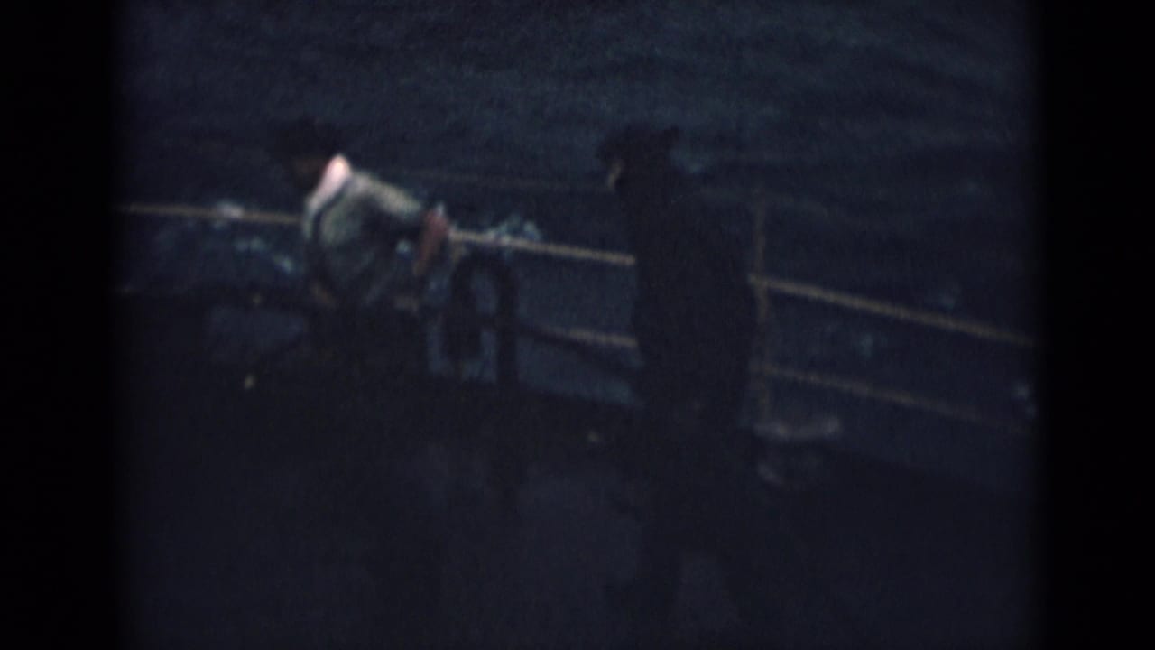 Sailor bends near a deck railing with dark water behind him.