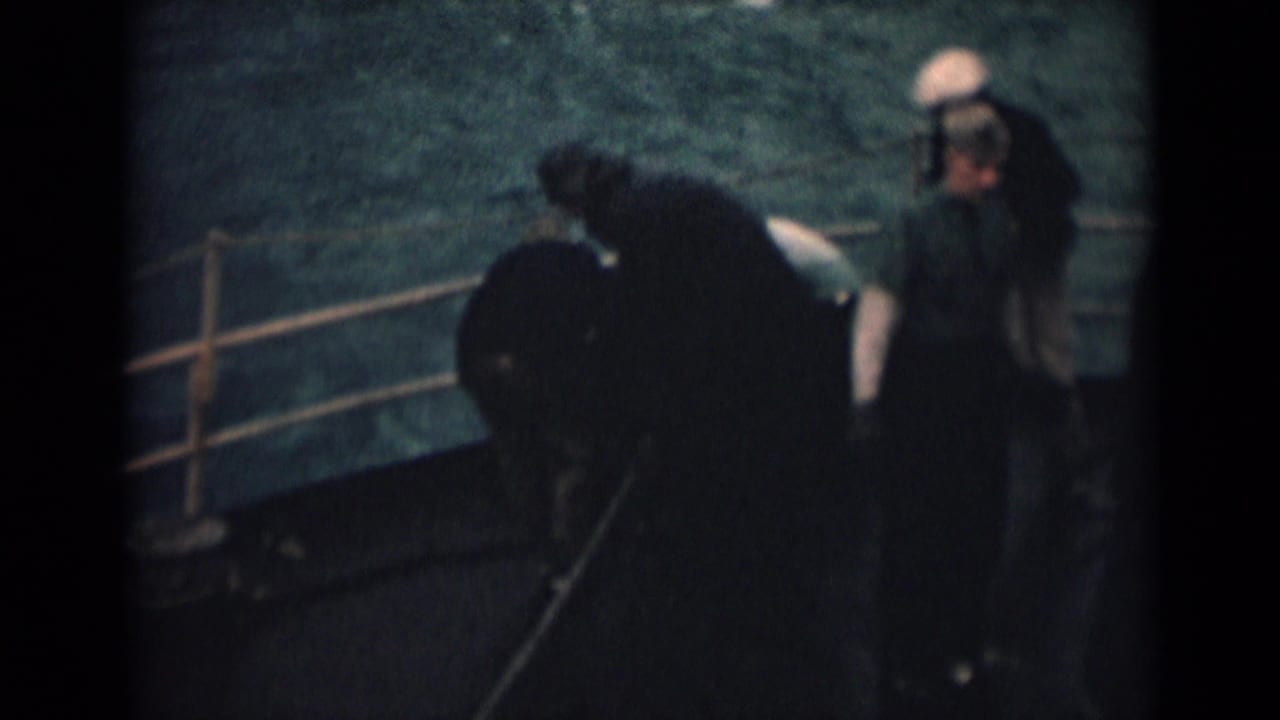 1946 8mm frame showing two sailors on a ship deck off India, one in a light cap and another in darker clothing.
