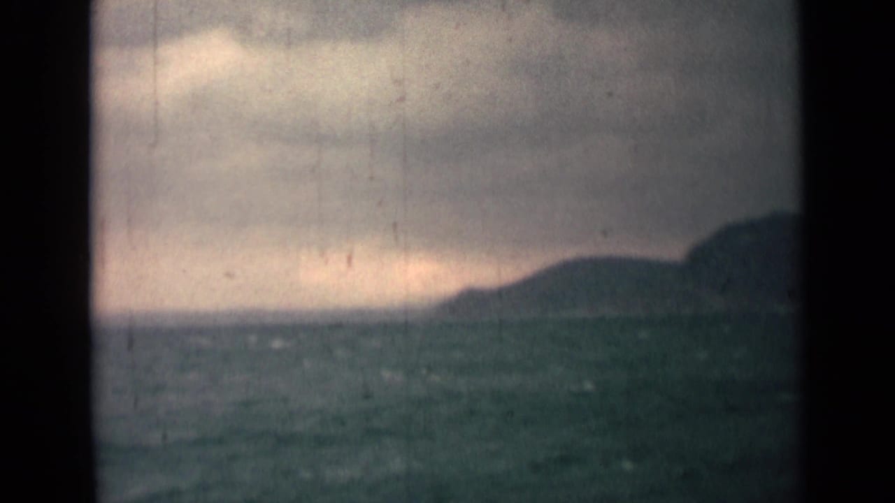 Distant coastline and rough water under an overcast sky on aged 8mm film.