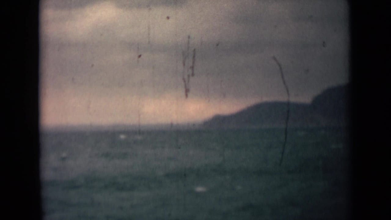 1946 India 8mm frame with choppy blue-green water, a hilly horizon, gray cloud cover, and prominent aged-film marks.