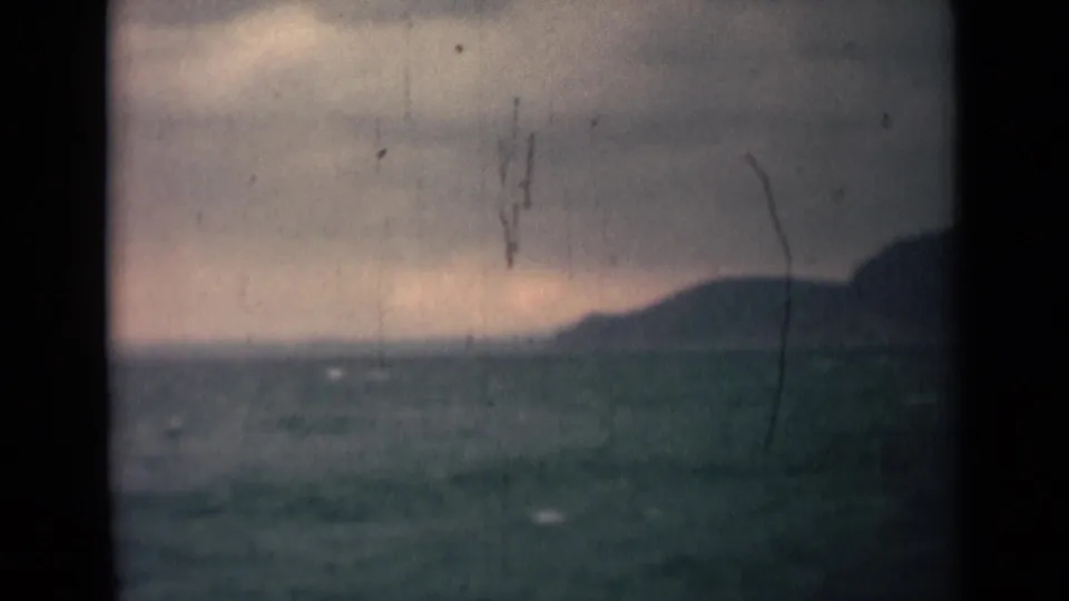 1946 India 8mm frame with choppy blue-green water, a hilly horizon, gray cloud cover, and prominent aged-film marks.