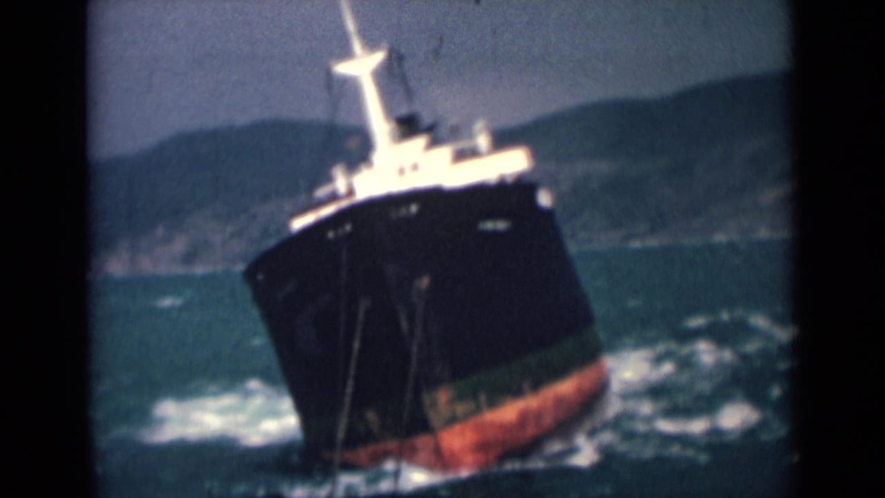1946 India 8mm frame showing a cargo ship with black hull, red lower section, and white superstructure listing in rough coastal seas.