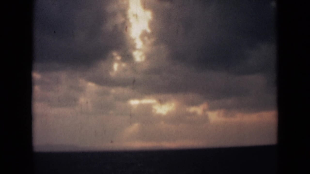Dramatic coastal sky over India with sunlight filtering through clouds and reflecting faintly on the water below.