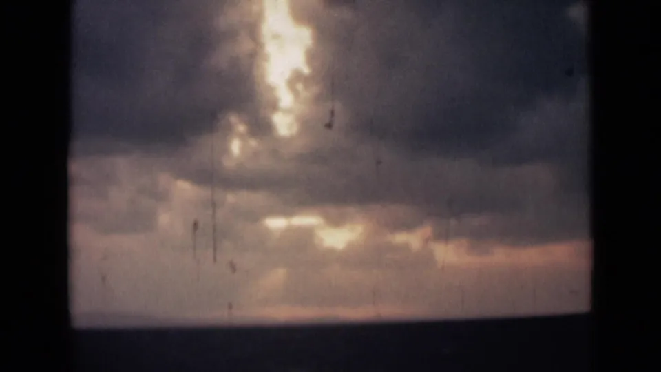 1946 India home-movie frame showing thick clouds lit by low sun over a distant dark horizon.