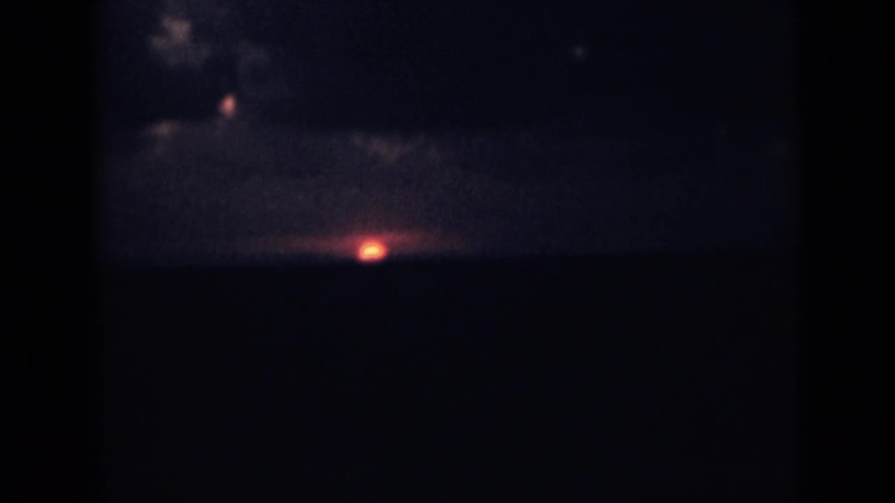 1946 India home-movie sunset frame with a small red sun low above a dark distant ridge.