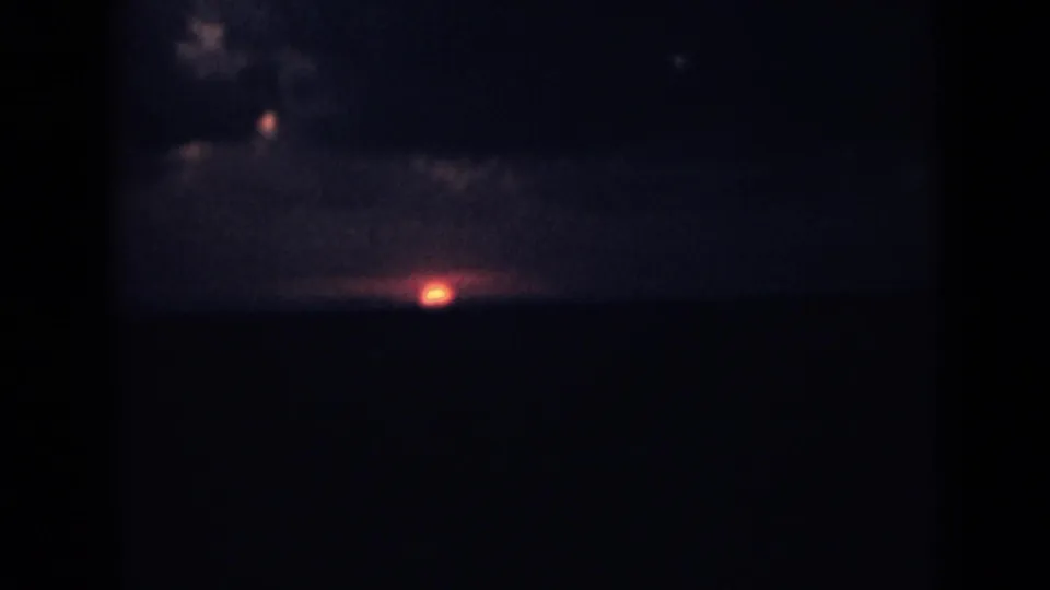1946 India home-movie sunset frame with a small red sun low above a dark distant ridge.