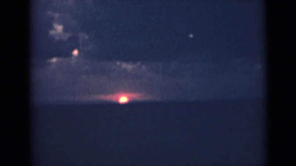 Archival 8mm sunset over India, with a red sun near the horizon below dark cloud cover.
