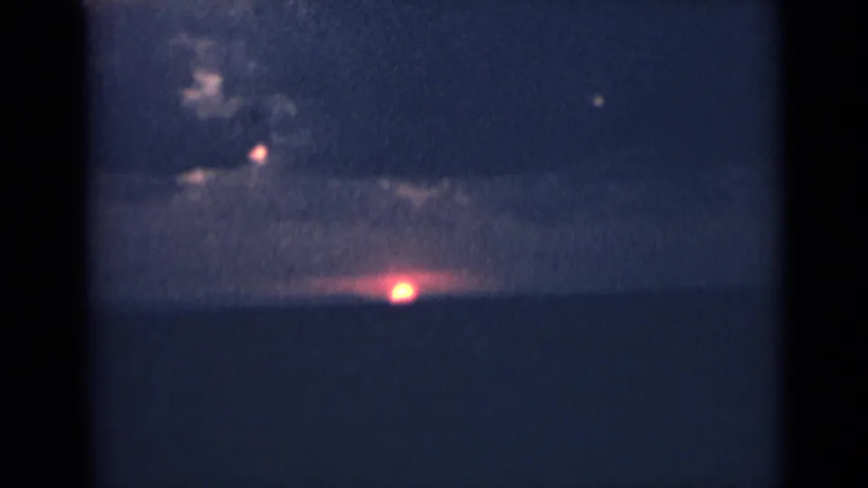 1940s India home-movie frame showing a dim horizon, cloud band, and bright low sun or light near the edge of the landscape.
