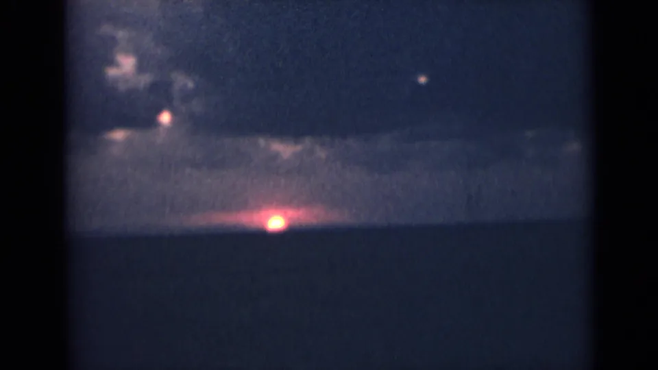 1940s India home-movie frame with a dark horizon, clouded sky, and a small bright glow near the lower center of the scene.