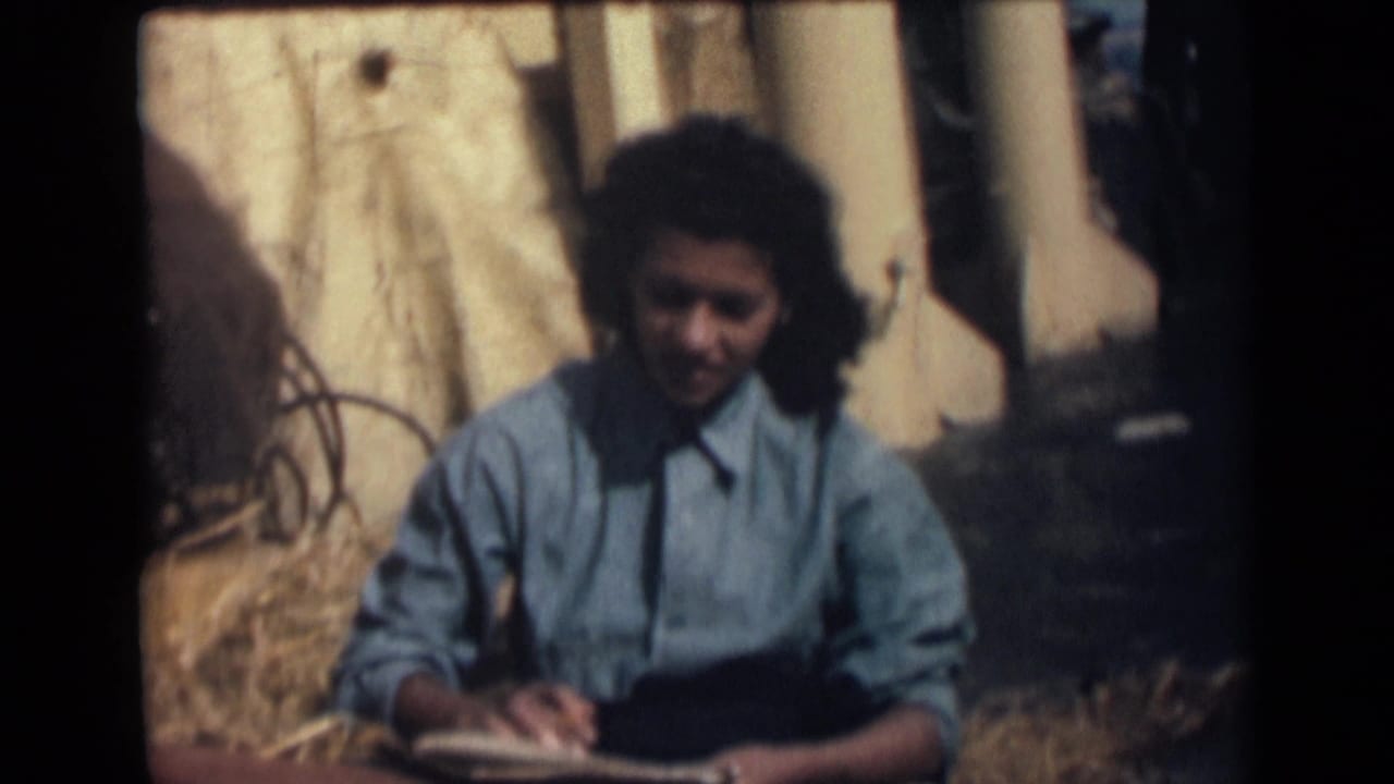 A girl in 1946 India appears focused on handwriting in an open notebook while seated outside in bright daylight.