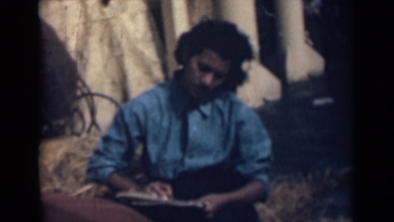 A girl in a blue shirt sits with an open notebook in 1946 India footage, with windblown hair and a rustic outdoor backdrop.