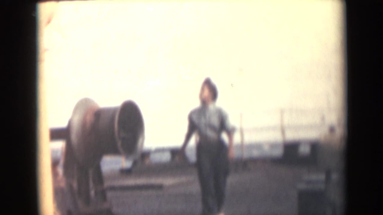 A woman walks across a ship deck near large propeller-like equipment in 1946 India-related 8mm footage.