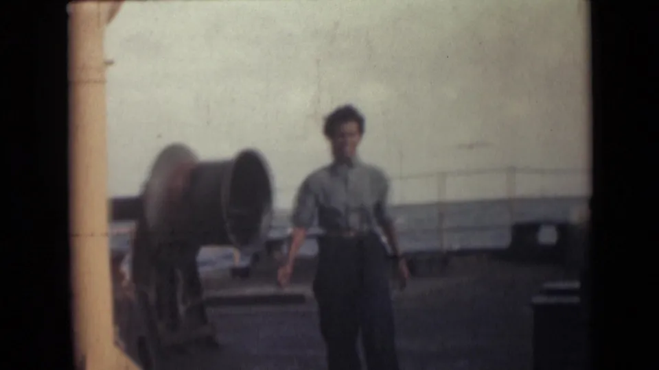 Woman on a ship deck near large marine equipment and railing in 1946 India-related 8mm footage.
