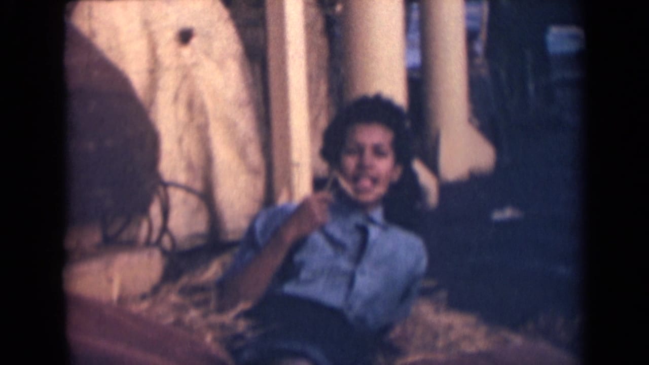 The woman sits or reclines on the ship deck, smiling toward the home-movie camera with columns and shadows behind her.