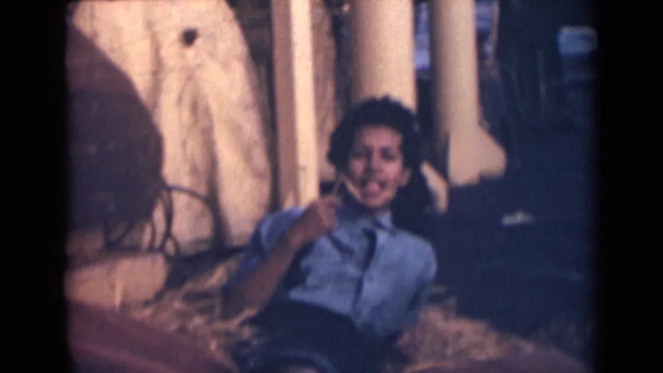 The woman sits or reclines on the ship deck, smiling toward the home-movie camera with columns and shadows behind her.