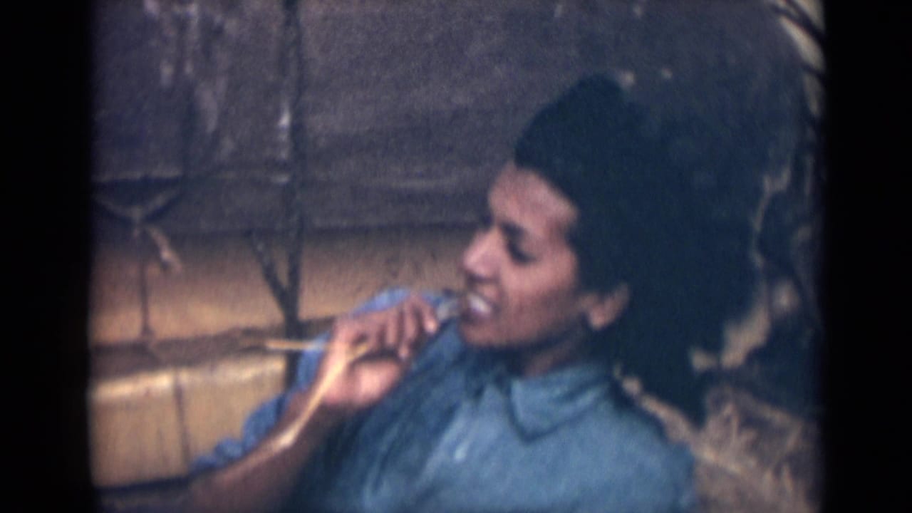 Young woman in a blue collared shirt holds an object near her mouth outdoors.