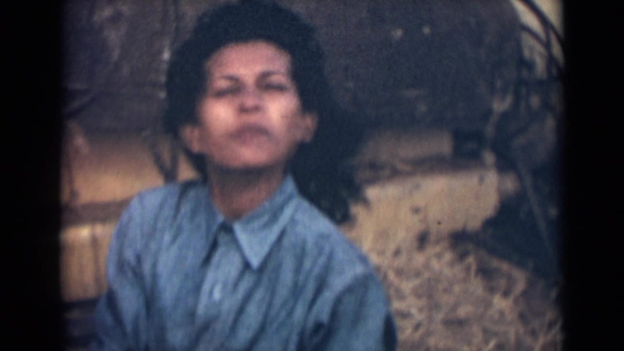 A young woman in 1946 India faces the camera in a blue collared shirt, framed closely against an earthy outdoor background.