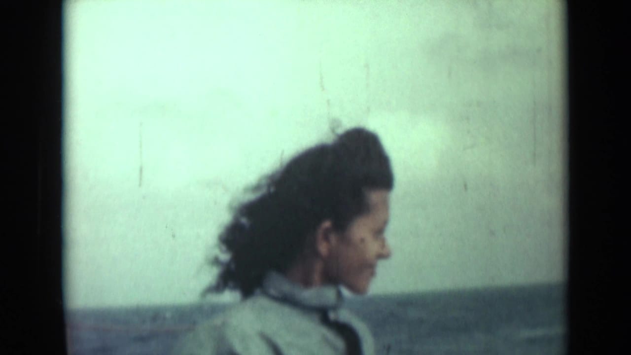 In a coastal 1946 India frame, the woman turns in profile near open water as wind pushes her dark hair back.