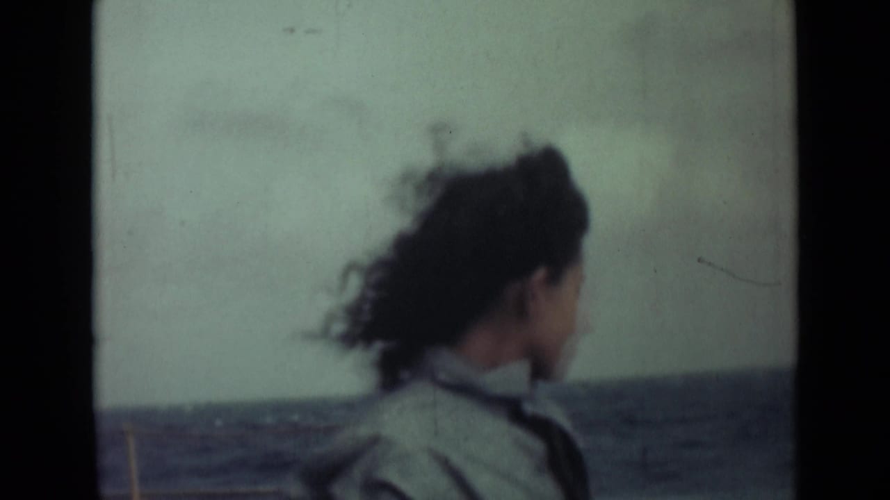 Woman in a light jacket seen in profile on a boat with water behind her.