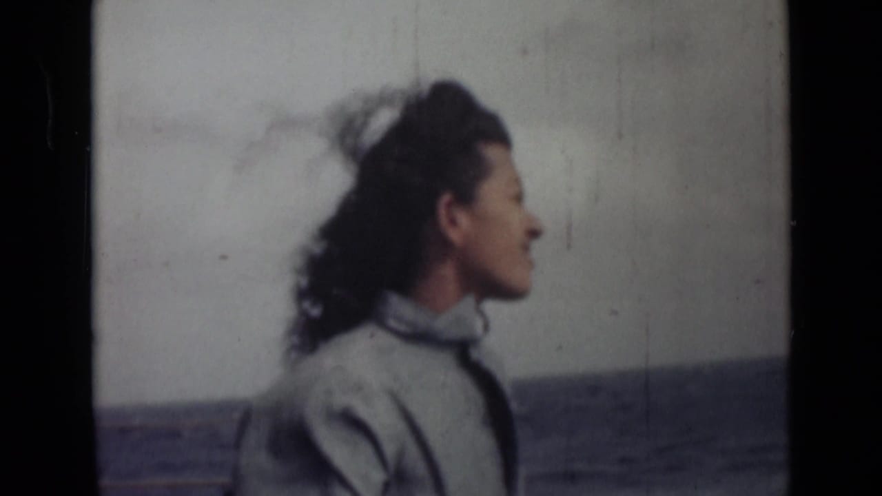 Woman smiles in side profile with windblown hair and water in the background.
