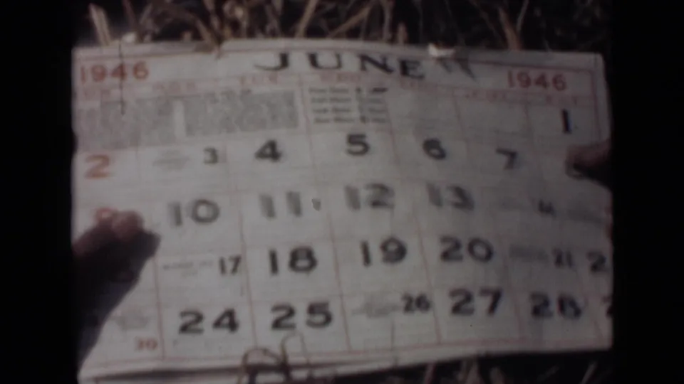 Hands hold a June 1946 calendar page close to the camera, with grass or brush visible behind it.