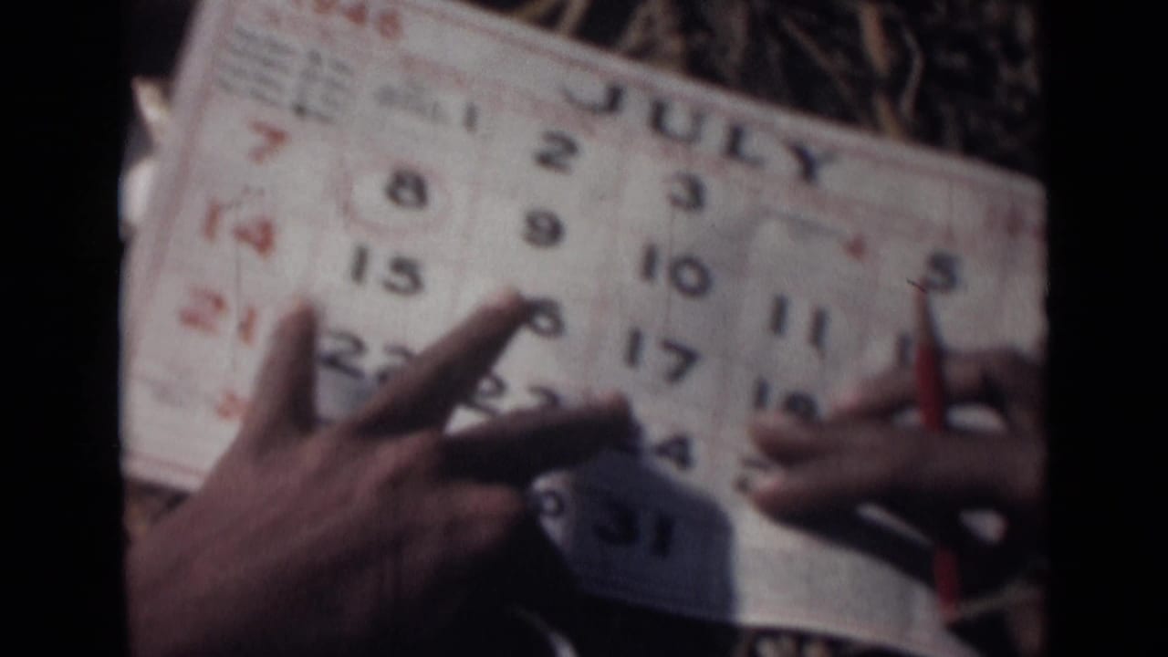 Hands hold a July 1946 calendar page while a pencil points near the numbered dates.