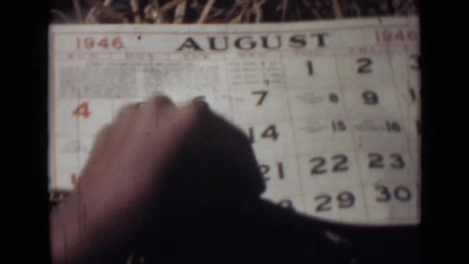 A hand presses against an August 1946 calendar page in this soft, grainy 8mm home-movie frame from India.